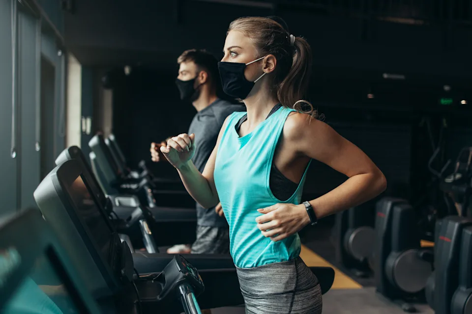 Young fit woman and man running on treadmill in modern fitness gym